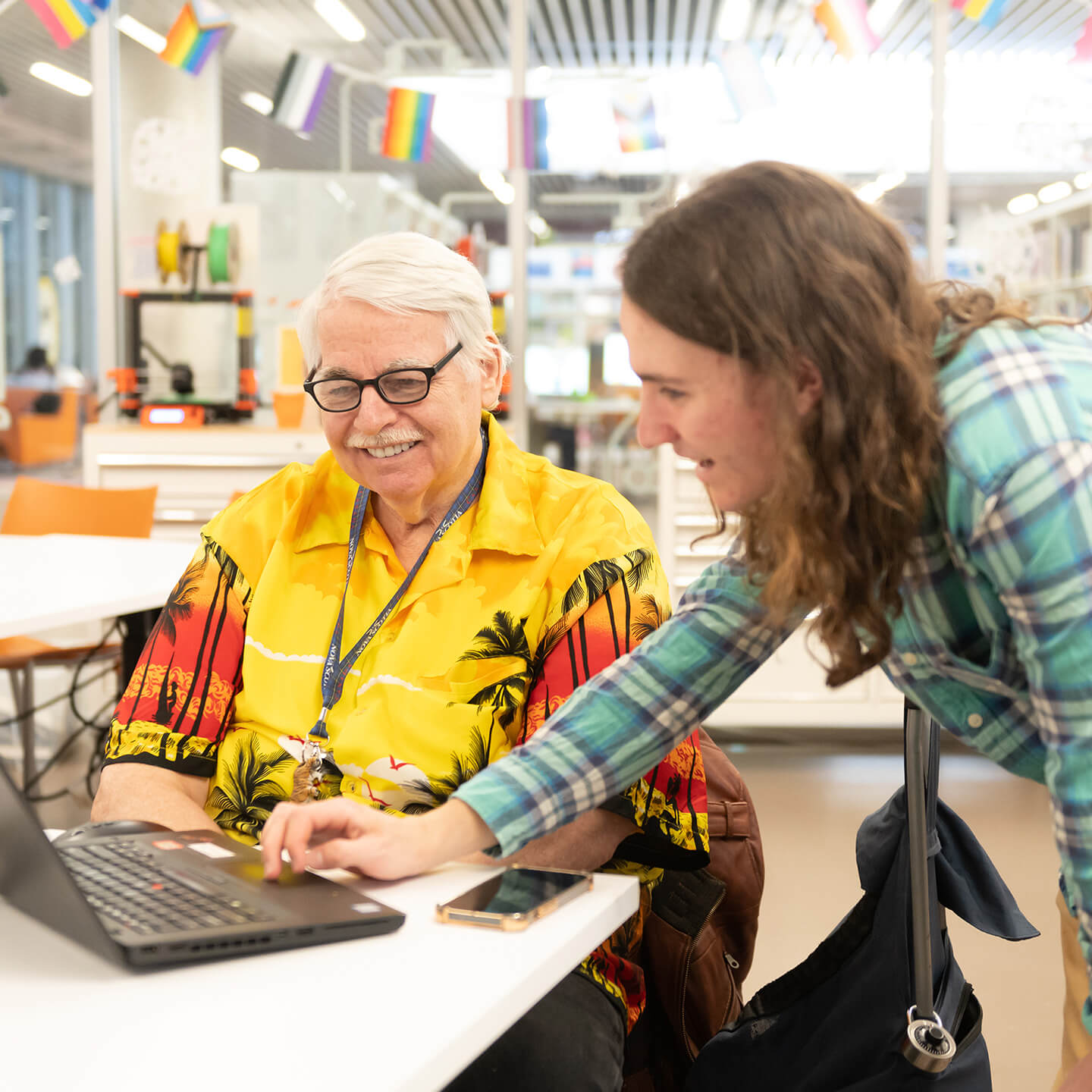 2 people and a laptop at the Library, one person is demonstrating or guiding the other.
